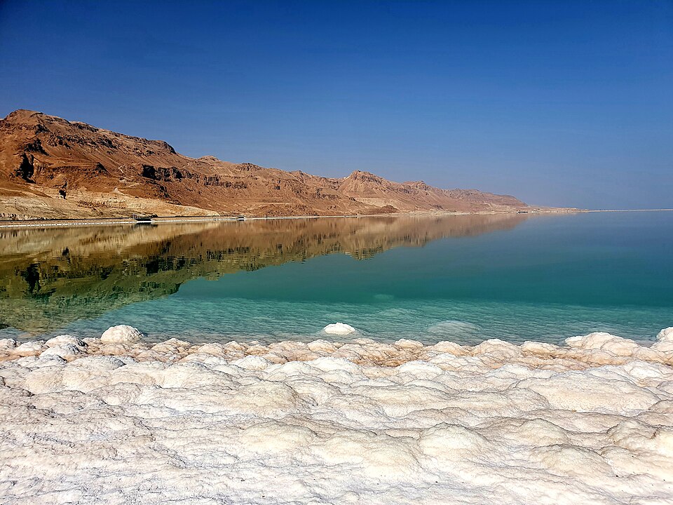 Turquoise Dead Sea water and white salt crust with mountains behind